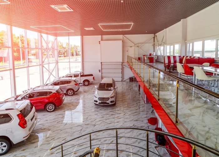 Top view of car dealership showroom with customers and salesmen. Modern glass building with brand new cars inside.